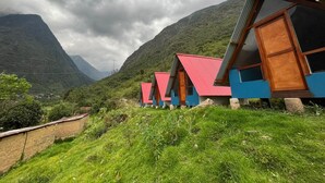 A row of cabins with red roofs and blue walls, set against a mountainous backdrop.