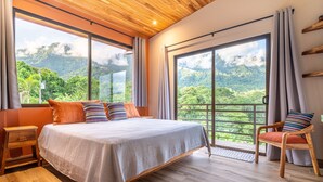 Un dormitorio con una cama grande, piso de madera y vistas a un follaje exuberante a través de las ventanas.