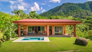 Una casa moderna con techo rojo, piscina y un jardín exuberante.