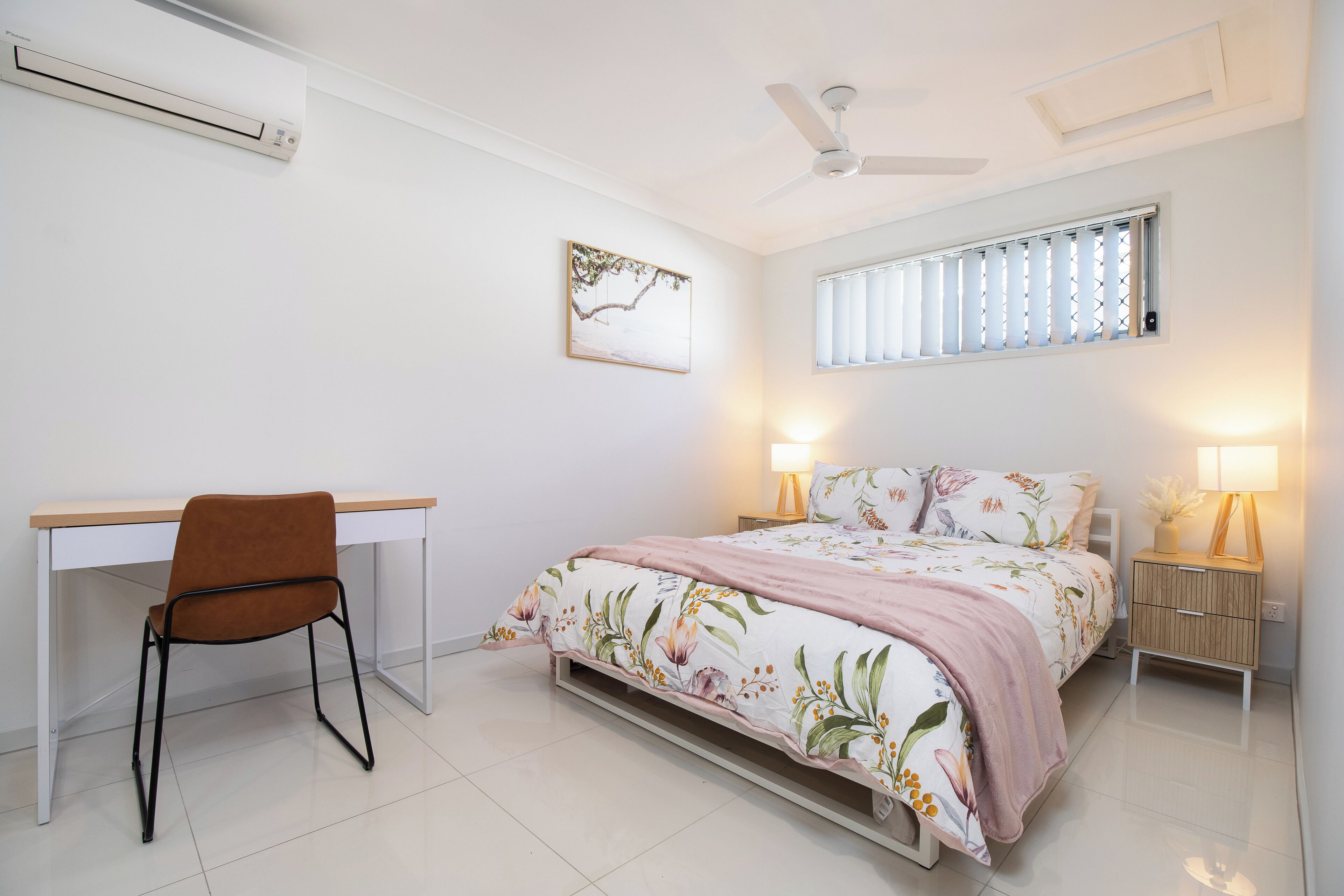 A bedroom with a bed, desk, chair, bedside lamps, and a ceiling fan.
