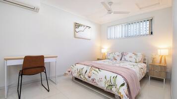 A bedroom with a bed, desk, chair, bedside lamps, and a ceiling fan.
