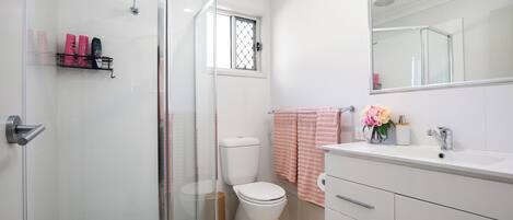 Un baño moderno con cabina de ducha de vidrio, inodoro blanco, tocador con espejo y toalla rosa.