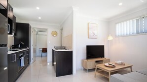 A modern kitchen with a central island, a dining area with a TV and table, and a living room with a sofa.