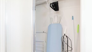 A laundry room with a drying rack, ironing board, and mops.