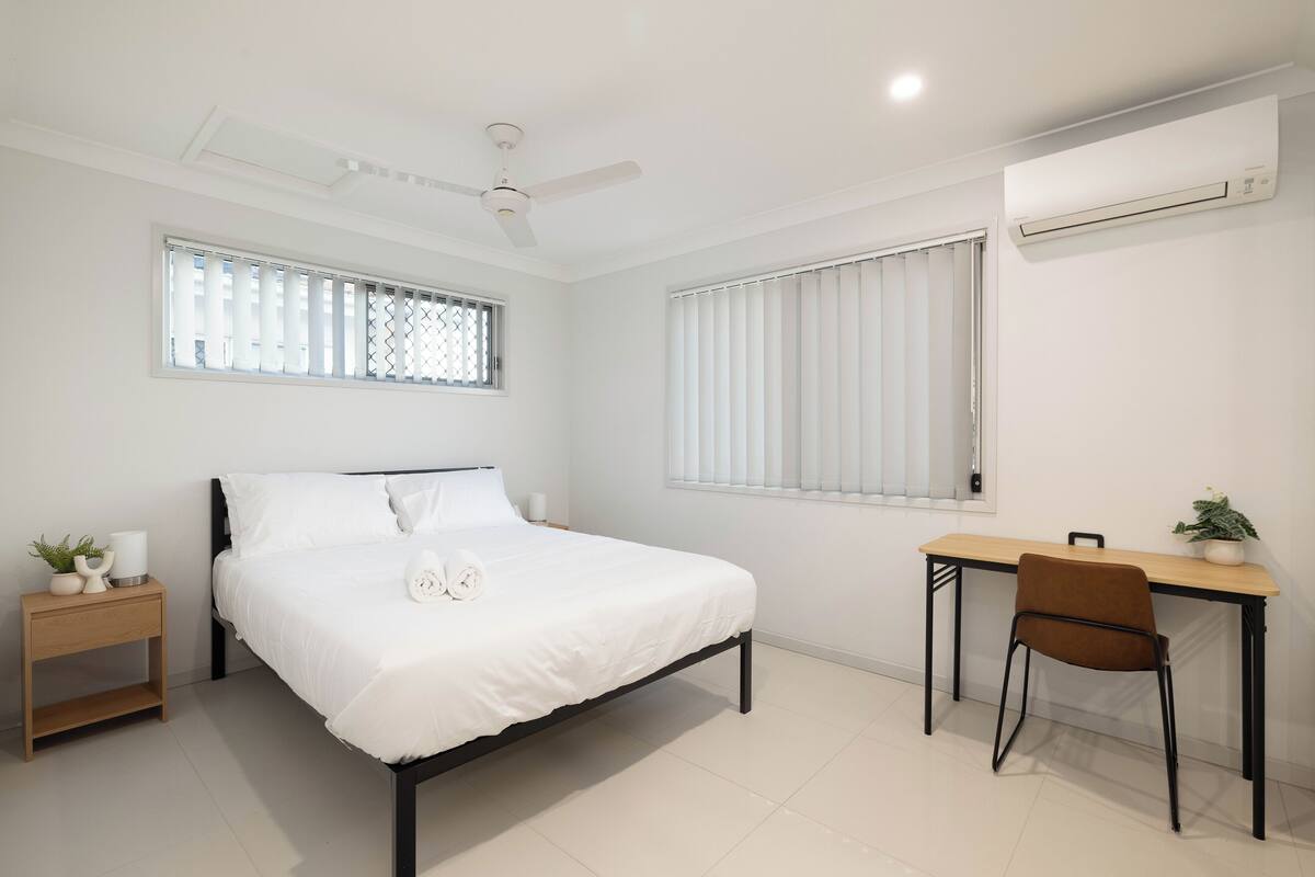 Une chambre à coucher comprenant un lit, un bureau, une chaise, un ventilateur de plafond et un appareil de climatisation.