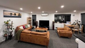 A modern living room with leather sofas, a flat-screen TV, a coffee table, and a dining area with a table and chairs.