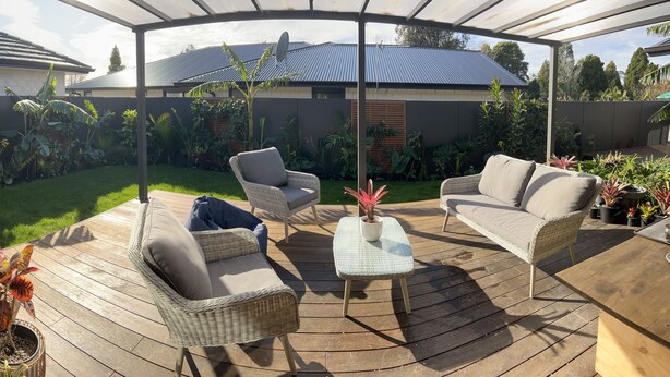 A covered outdoor patio with wicker furniture, a small table, and various potted plants.