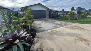 A residential driveway with a garage, surrounded by various plants and a clear sky.