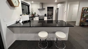 A modern kitchen with a black countertop, white cabinets, and two white bar stools.