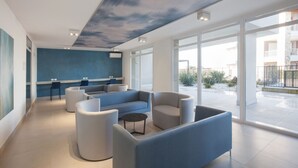 A modern lobby with a blue wall, comfortable seating, and large windows offering a view of the outside. - Perla Garda Lake Apartment With Pool (Peschiera del Garda)