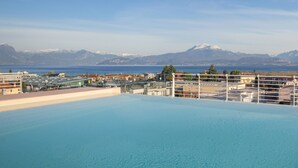 A rooftop pool with a view of a cityscape and mountains in the background. - Perla Garda Lake Apartment With Pool (Peschiera del Garda)