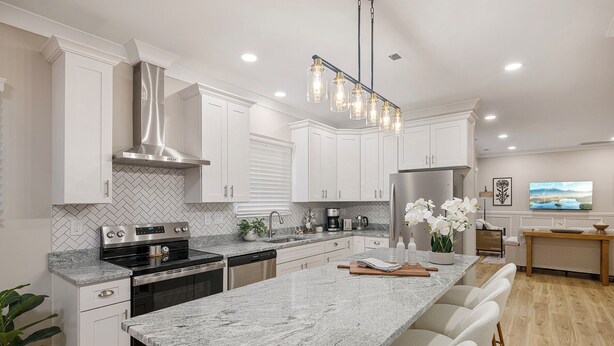 A modern kitchen with white cabinetry, a granite countertop, stainless steel appliances, and a central island with bar stools.