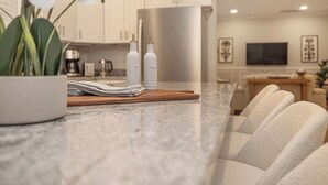 A modern kitchen with marble countertops, two bottles labeled "OIL" and "VINEGAR," and a potted orchid.