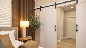 A bedroom with a bed, a bedside lamp, a potted plant, and a sliding door leading to another room.