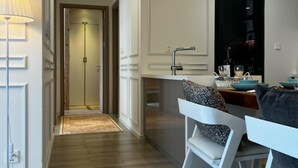 Een moderne keuken met witte kasten, een eethoek met witte stoelen, en een gang naar een deur.