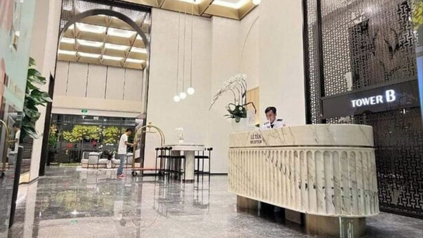 Een moderne hotel lobby met een receptiebalie, een grote bogenpoort en een bord met 'TOWER B'.
