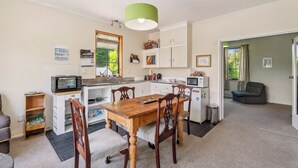 A compact kitchen with a wooden dining table, white cabinets, and a green pendant light. - Riverside Retreat in beautiful Arrow Junction (Arrow Junction)