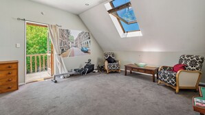 A room with a sloped ceiling, a skylight, a large window, a chair, a table, a dresser, and a door leading to a balcony. - Riverside Retreat in beautiful Arrow Junction (Arrow Junction)
