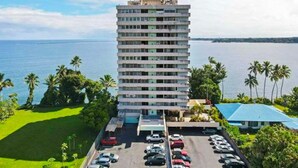 A tall hotel with multiple floors, a parking lot, and a view of the sea.