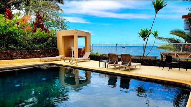 A pool area with lounge chairs and a small structure, overlooking a body of water.
