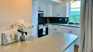 A modern kitchen with white cabinets, a black stove, and a view of greenery outside.