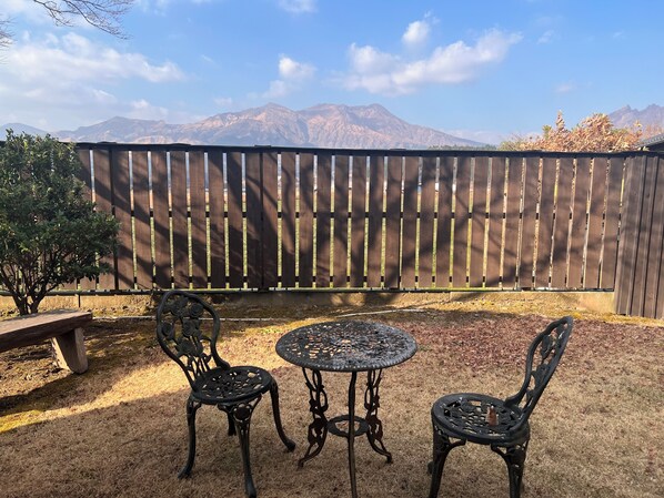 Eine Terrasse mit zwei Metalltischen und -stühlen, einem Holzzaun und Blick auf Berge.