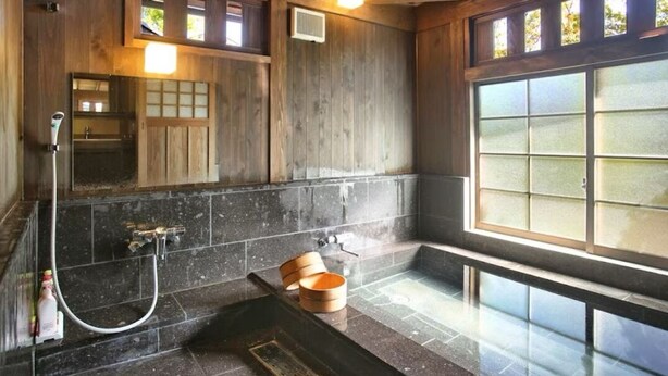 Un bagno in stile tradizionale giapponese, con interni in legno, un'ampia finestra e un pavimento in pietra.