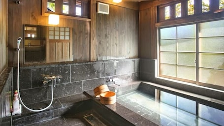 A traditional Japanese-style bathroom with a wooden interior, a large window, and a stone-tiled floor.