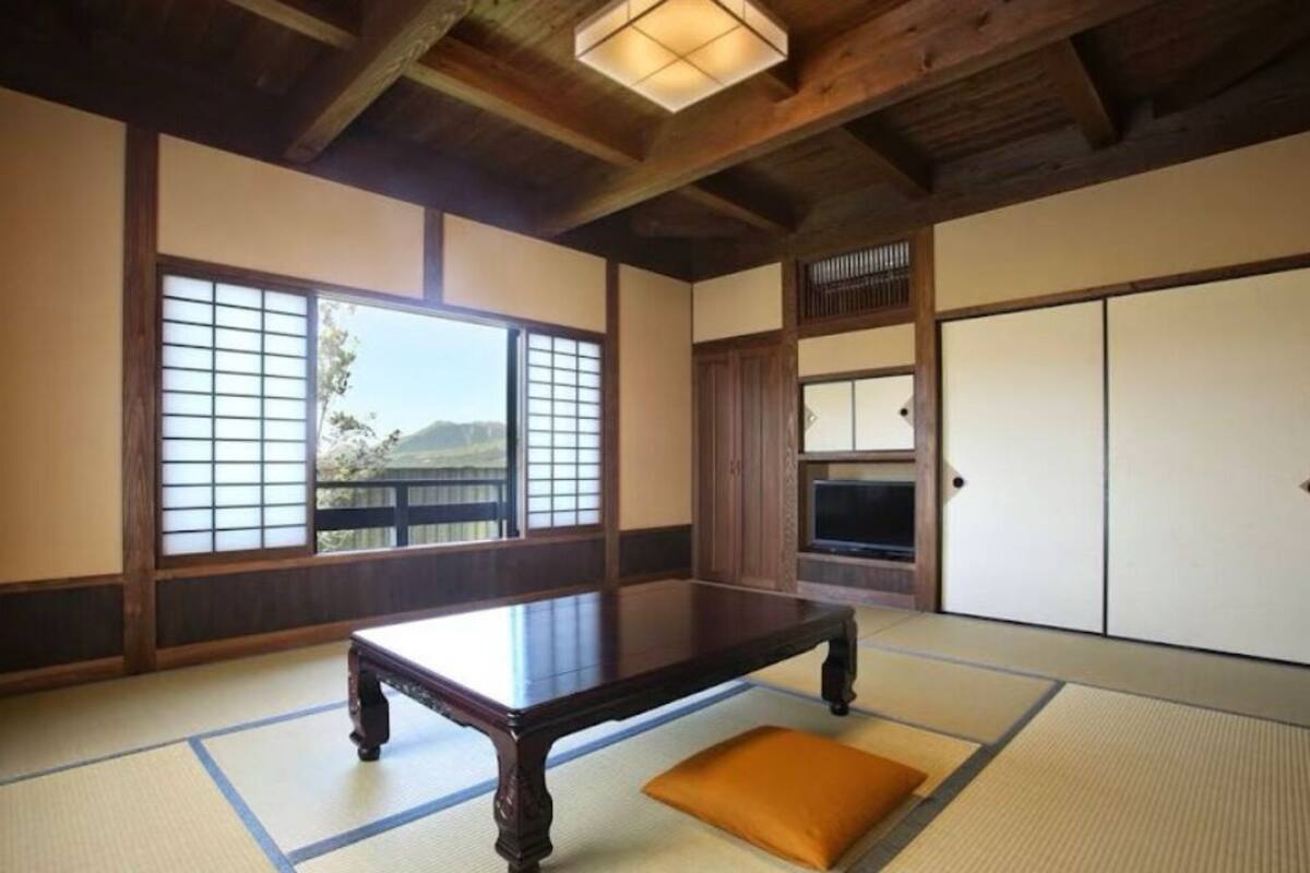 A traditional Japanese room with tatami flooring, a low wooden table, sliding doors, and a view of the outdoors.