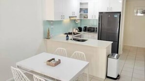 A compact kitchen with white cabinets, a stainless steel refrigerator, a microwave, and a sink. There is a small dining table with chairs. - Central location | Alfresco dine on huge terrace | Walk to cafes/shops/blowhole (Kiama)