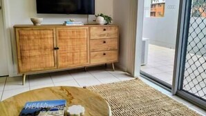 A living room with a wooden cabinet, a television, and a view through a glass door. - Central location | Alfresco dine on huge terrace | Walk to cafes/shops/blowhole (Kiama)
