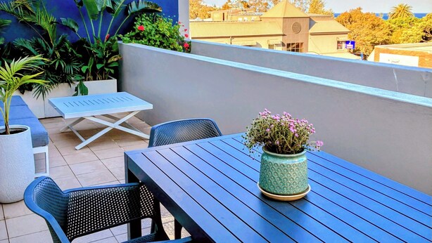 A rooftop terrace with a table and chairs, potted plants, and a view of the cityscape. - Central location | Alfresco dine on huge terrace | Walk to cafes/shops/blowhole (Kiama)