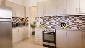 A modern kitchen with light wood cabinets, a stainless steel refrigerator, a microwave, a coffee maker, and a built-in oven.