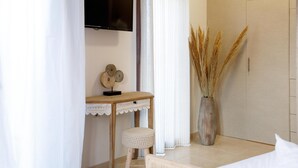 A bedroom with a bed, a bedside table with a decorative item, a television mounted on the wall, and a vase with dried plants.