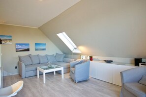 Un soggiorno moderno e luminoso, con soffitto alto, un divano, un tavolino da caffè e una postazione scrivania.