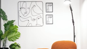 Una sala de estar moderna con un sillón naranja único, una lámpara de pie negra y arte abstracto en la pared.