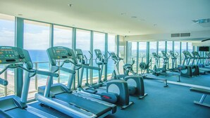 Un gimnasio con máquinas de cardio, una banca de pesas y grandes ventanales con vista al océano.