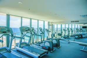 Une salle de sport équipée de machines de cardio, d’un banc de musculation et de grandes fenêtres donnant sur l’océan.