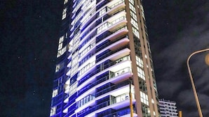 Un hotel moderno y alto, con fachada curva, varios balcones y un área de entrada bien iluminada.