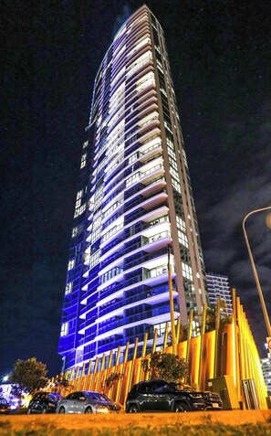 A tall, modern hotel with a curved facade, multiple balconies, and a well-lit entrance area.