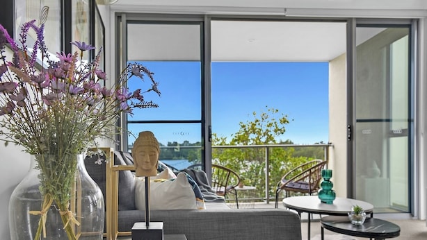 A modern living room with a sofa, a table, and a vase of flowers. - Tri-Level 2BR Water-View Townhouse | Free Parking (Carrara)