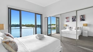 A modern bedroom with a large bed, a mirror, and a view of a lake. - Tri-Level 2BR Water-View Townhouse | Free Parking (Carrara)