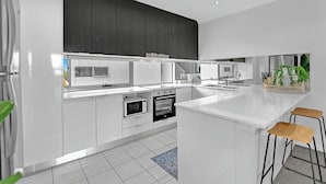A modern kitchen with white cabinetry, stainless steel appliances, and a central island with bar stools. - Tri-Level 2BR Water-View Townhouse | Free Parking (Carrara)