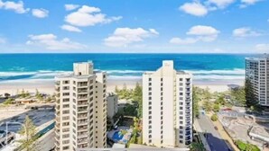 A coastal view of a high-rise hotel with multiple floors, a beach in the background, and a clear sky. - Ocean View King Bed Studio | Steps to Beach and Tram (Surfers Paradise)