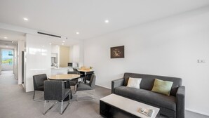 Een moderne woonkamer met een grijze bank, een ronde salontafel en een eethoek met een kleine tafel en stoelen.