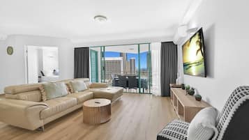 A modern living room with a beige sectional sofa, a round coffee table, and a view of a cityscape through large glass doors.