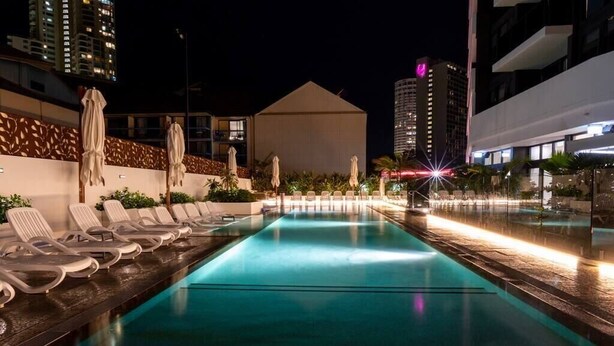 A nighttime pool area with lounge chairs and umbrellas, surrounded by buildings. - Cozy and Bright 2-bedroom Apartment in Surfers (Surfers Paradise)