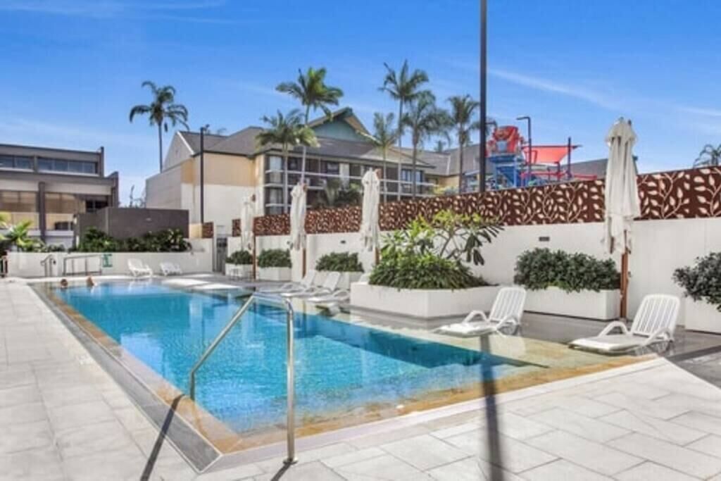 Una piscina con sillas de descanso, palmeras y un edificio moderno al fondo.