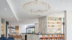A modern hotel lobby with a marble reception desk, bar area with bar stools, a chandelier, and a dining area with tables and chairs. - Cozy and Bright 2-bedroom Apartment in Surfers (Surfers Paradise)