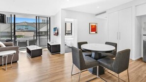 A modern kitchen with white cabinets, a round dining table, and grey chairs. - Cozy and Bright 2-bedroom Apartment in Surfers (Surfers Paradise)